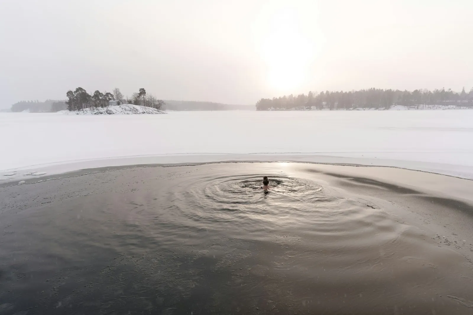 A person in a patch of open water surrounded by ice and snow