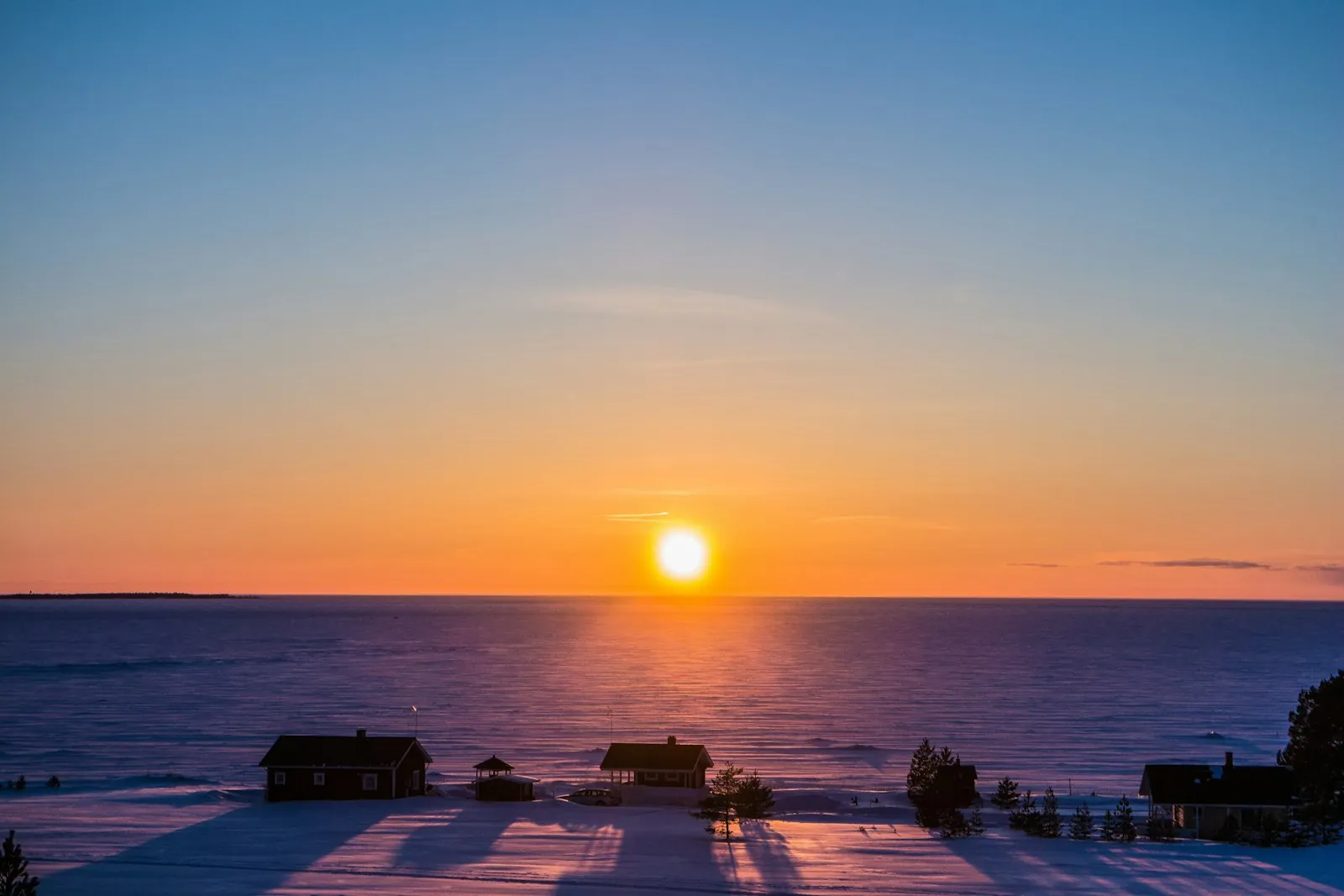 Sun setting over a frozen sea behind houses on the shore